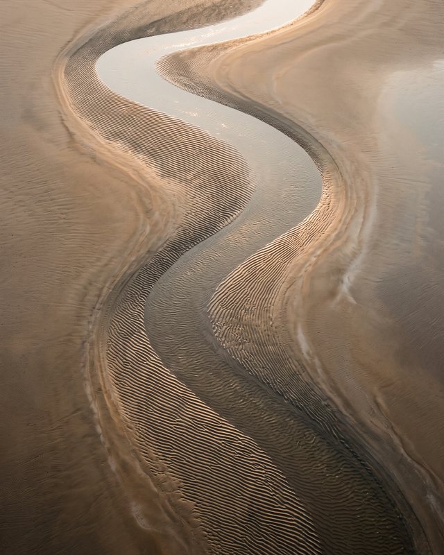 Estran de sable vu du ciel, sillon d'eau en méandre aux tons dorés