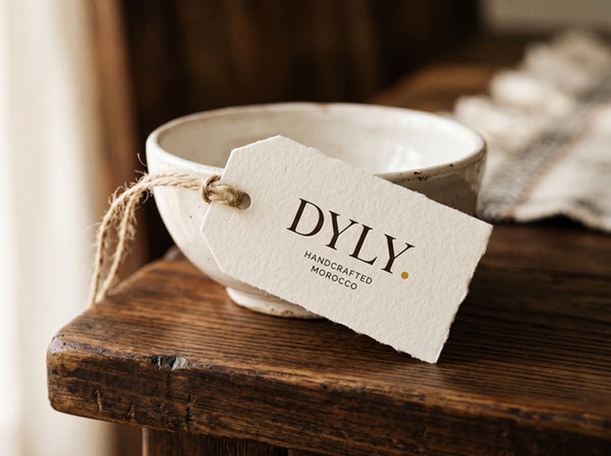 Étiquette DYLY nouée sur un bol en céramique artisanale, posée sur une table en bois — la marque appliquée directement sur la pièce vendue